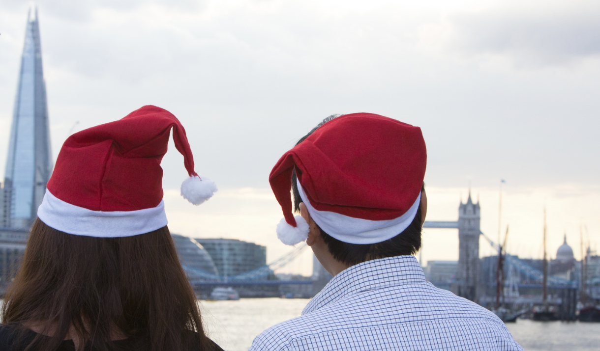 A couple wearing Santa hats look at the view of London including The Shard while on board City Cruises